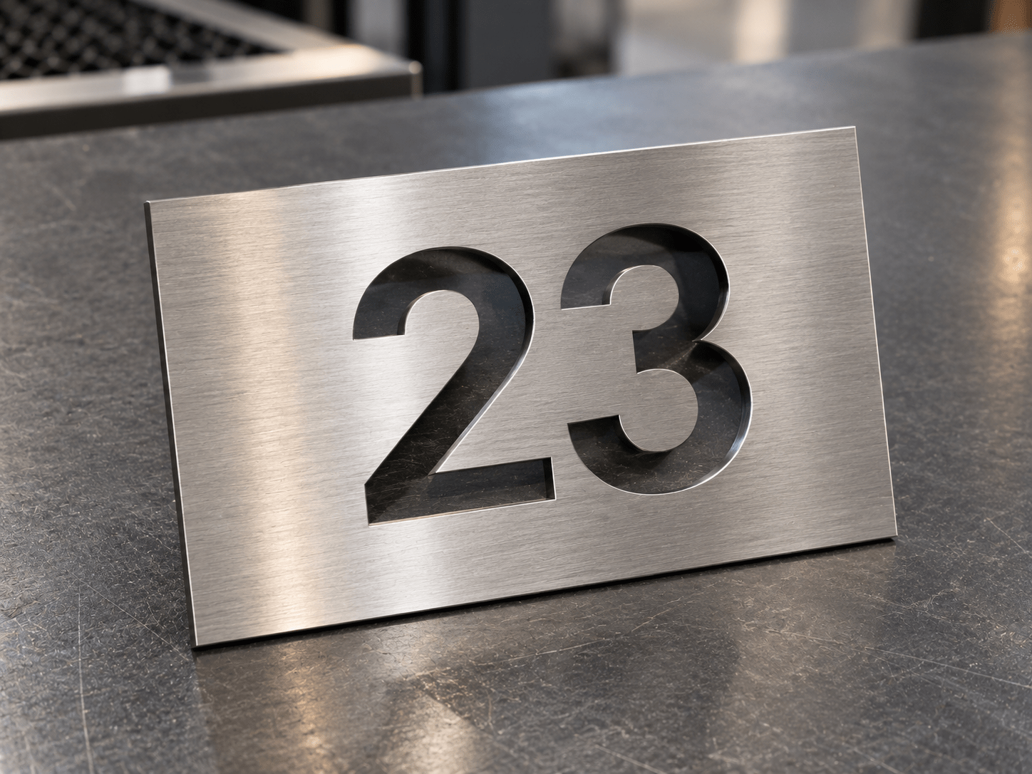 numéro de maison inox brossé découpe laser Plaque de numéro de maison « 23 » en inox brossé, découpée au laser dans une plaque rectangulaire en métal.